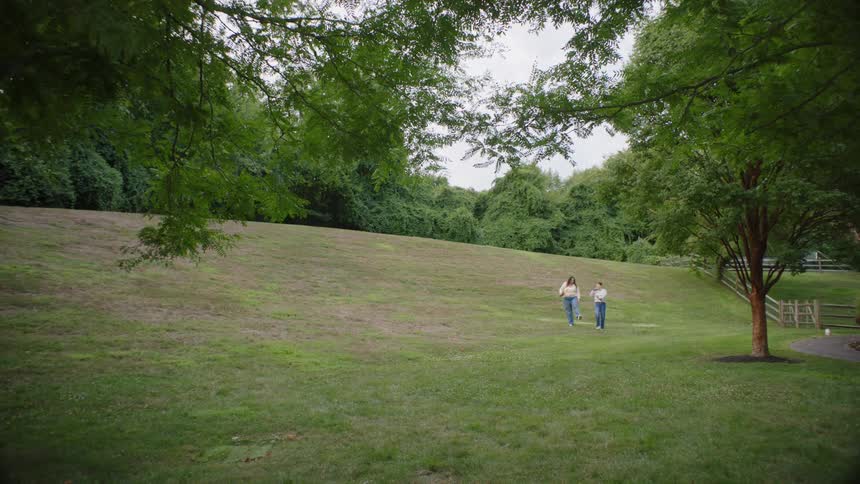 Two women walking through a public park with grass and trees