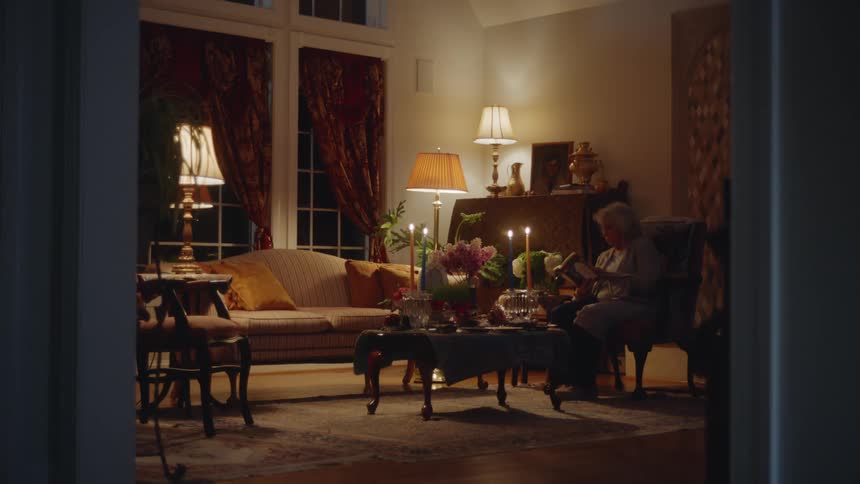 Elderly lady sitting in an armchair in the living room reading at night