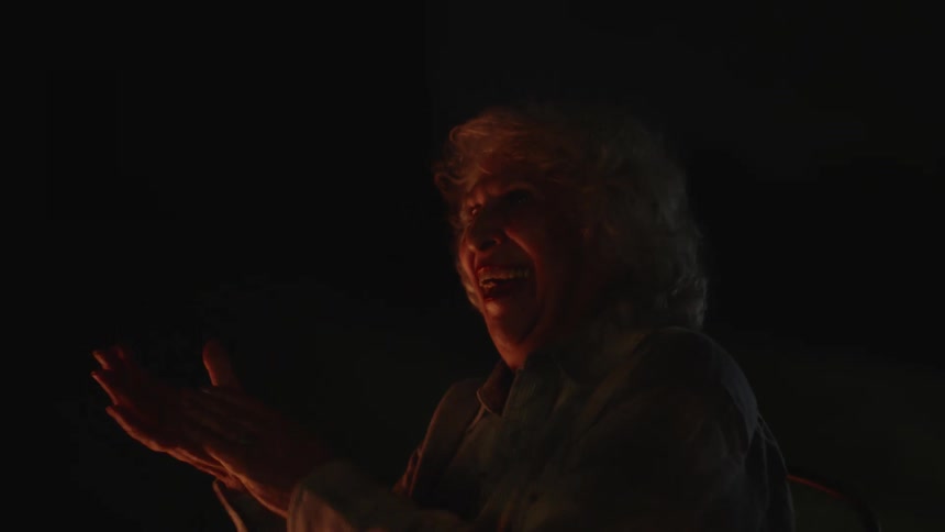 An elderly woman outdoors at night laughing and clapping her hands