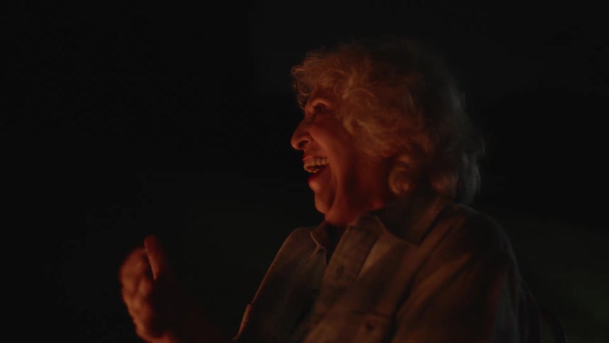 Elderly lady in an outdoor setting at night clapping her hands cheerfully