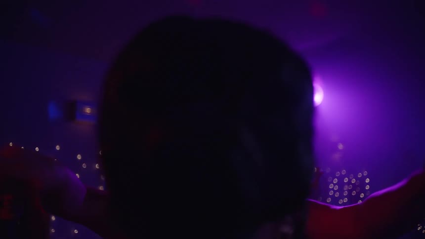 Women dance together at a party lit by colored lighting