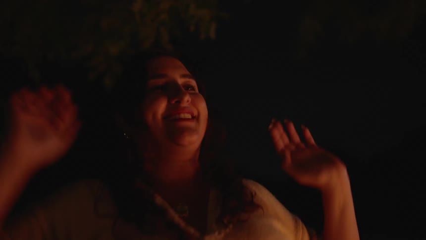 A woman jumps up and down her arms in the air smiling and celebrating before clapping her hands