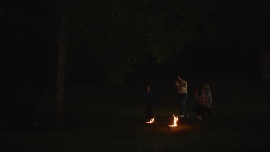 Friends camping in a field at night with two campfires jump over both fires