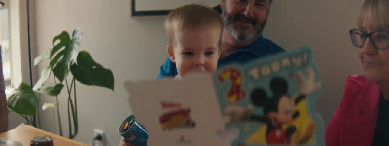 Young child looking at a book with grandparents and family nearby