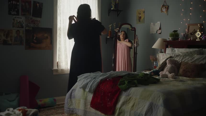 Woman in bedroom trying on a pink dress in front of a mirror