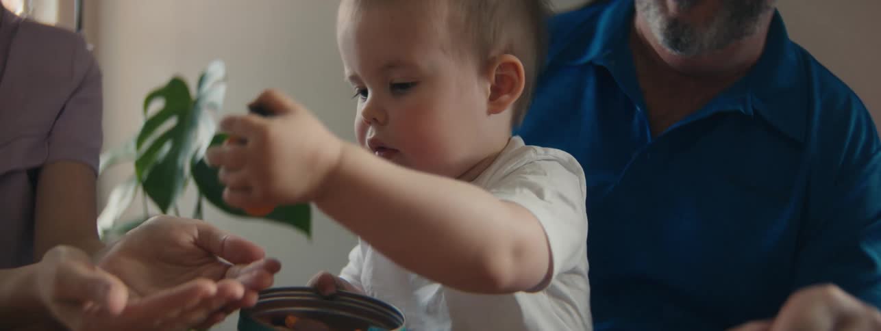 A grandfather and mother give a toddler sweets by pouring them into a tin