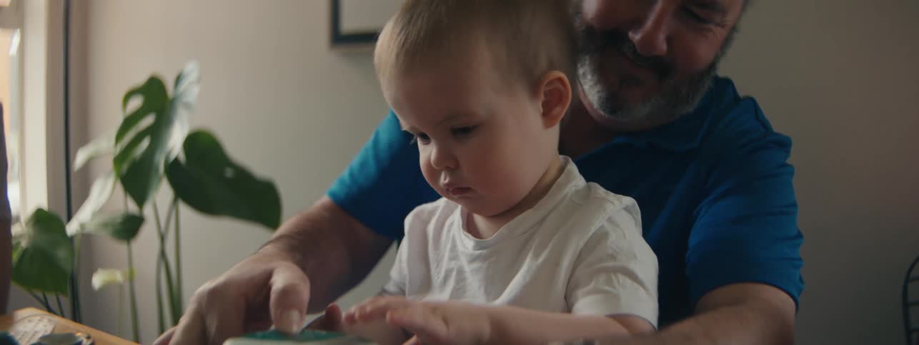 A grandfather helps a toddler with a package while his mother looks on
