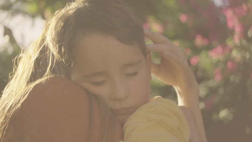 A mother hugs her sleeping son as she gently strokes his hair outdoors