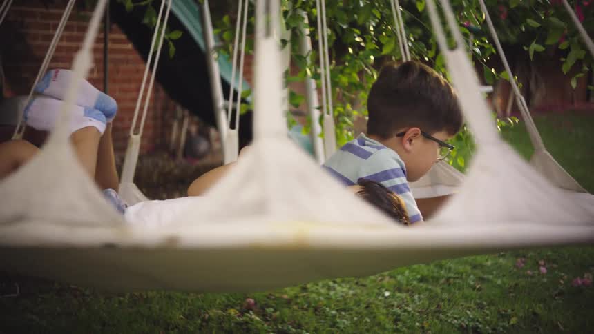 Two children lying on a white spinning hammock in the backyard