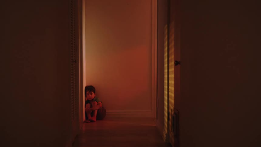 Little boy sitting in hallway of house scared by red light flashing next to him