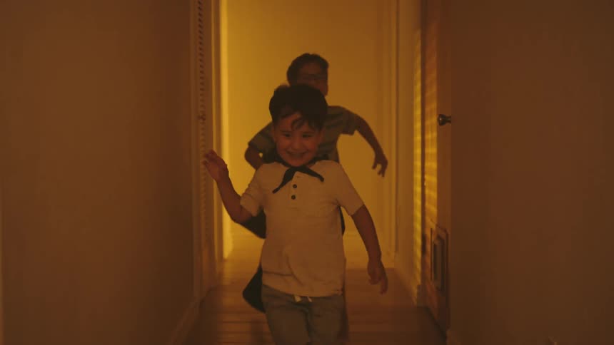 Boys wearing capes run through a hallway at home