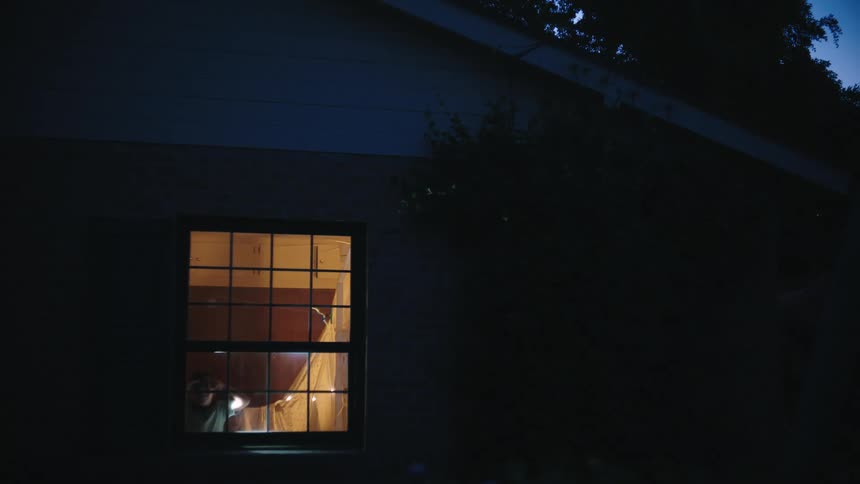View outside the window of a house at night and two children with a flashlight watching