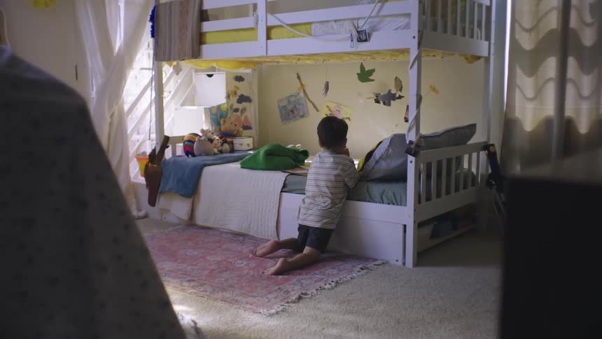 A young boy kneels on the floor in front of a bunk bed