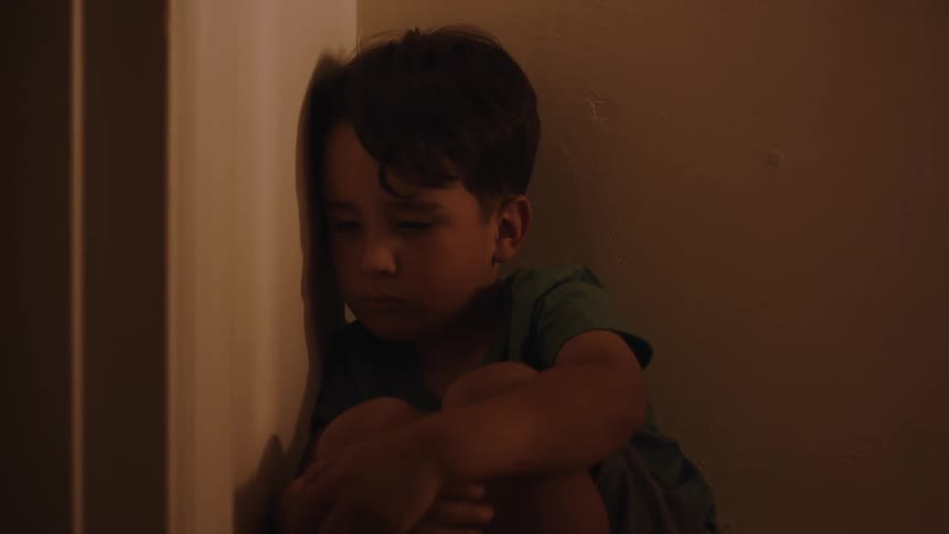 Little boy sitting in the corner of the wall