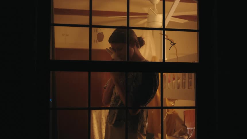Woman standing near a window at night cuddles a stuffed rabbit