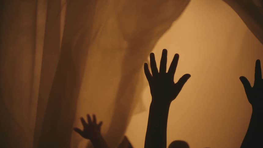 Two children are lying on a canopy bed and touching its blowing curtains