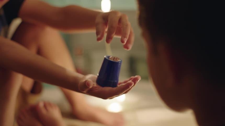 A boy performs a magic trick for his friend involving a plastic cup and coins