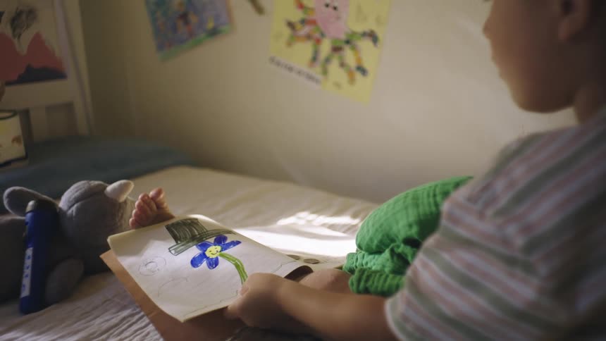 Boy sitting on bed looking at drawings in a book