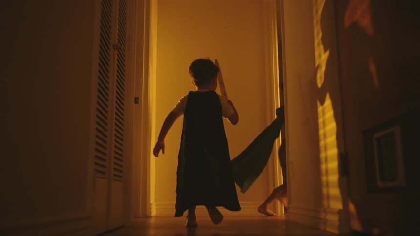 Two boys running down the hallway of the house playing with swords