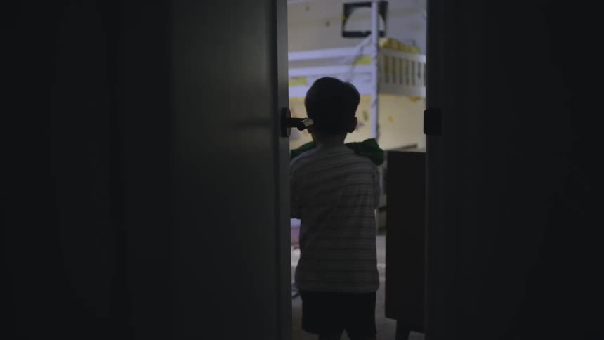 Boy carries clothes into a bedroom and places them on the lower of two bunk beds