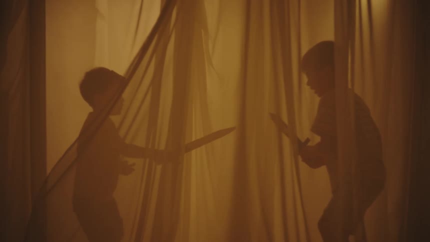 Two children playing with toy sword between curtains