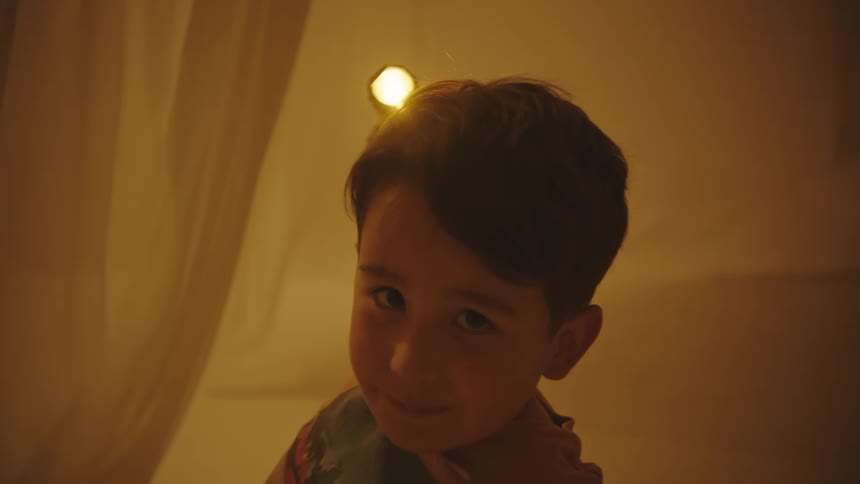 A young boy smiles as he holds a flashlight up over his head