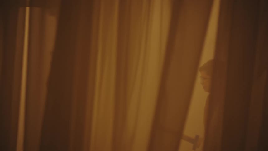 Two little boys running around playing between sheets and curtains