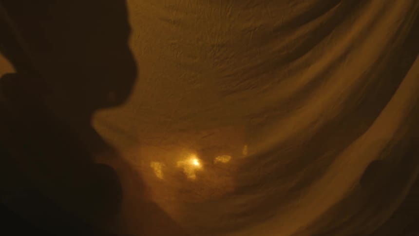 Shadow of a boy on a sheet reflecting a moving lamp in a dark room