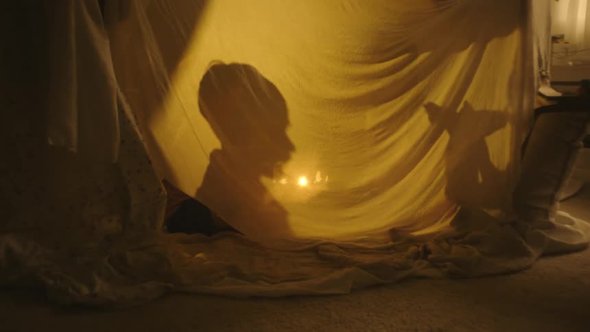 Shadow of two boys reflected in a sheet playing in the bedroom