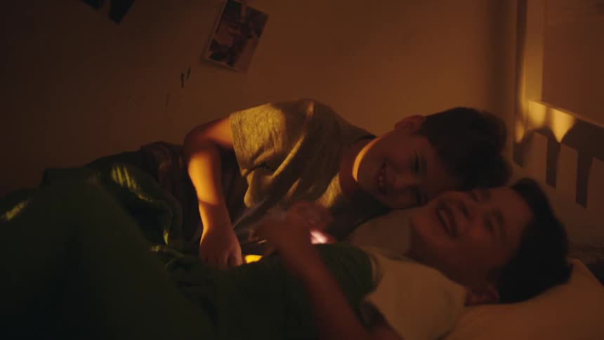 Two young boys are lying in bed and playing with a flashlight