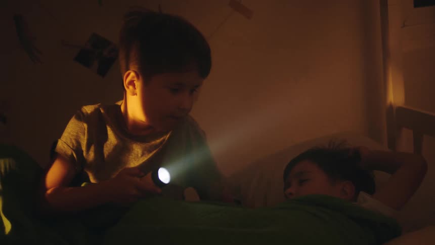 One brother wakes up in bed and turns on a flashlight and then lies back down next to his brother