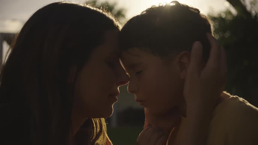 A mother gently rubs her sons head while theyre out in a yard