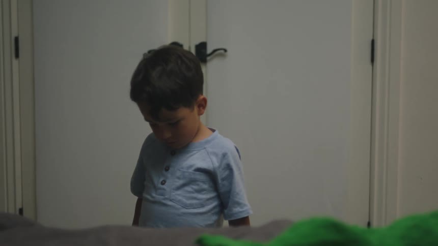 A young boy is sleeping in bed while another boy jumps into the bed with a flashlight