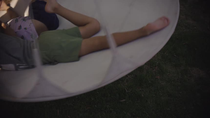 Two brothers spin around on a white circular swing as reflected light shines on the grass