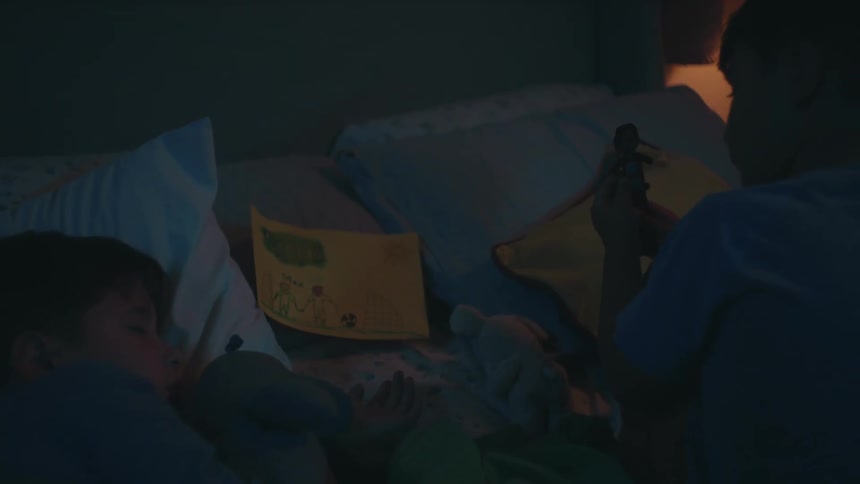 Two boys in a room with one of them sleeping and the other next to him building a doll
