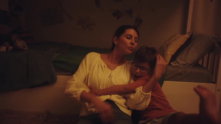 Mother and son hugging while sitting next to a bed in the bedroom