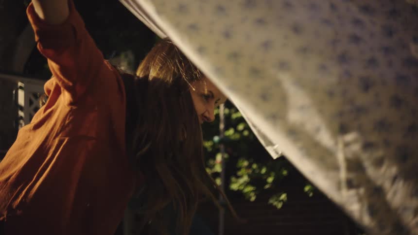 A laughing woman waves a sheet around in a yard