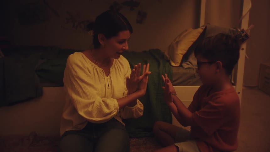 Mother sitting next to her son playing at making a dove gesture with her hands