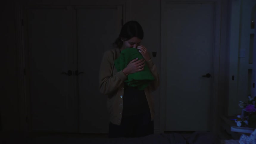 Woman in a dark room smelling a green blanket