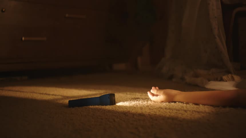 One child drops a flashlight and collapses on the floor while another runs out of the room in the evening