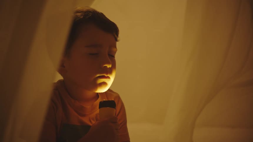 Boy sitting with his eyes closed with a flashlight on his face