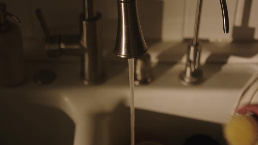 Woman turns off flowing kitchen faucet