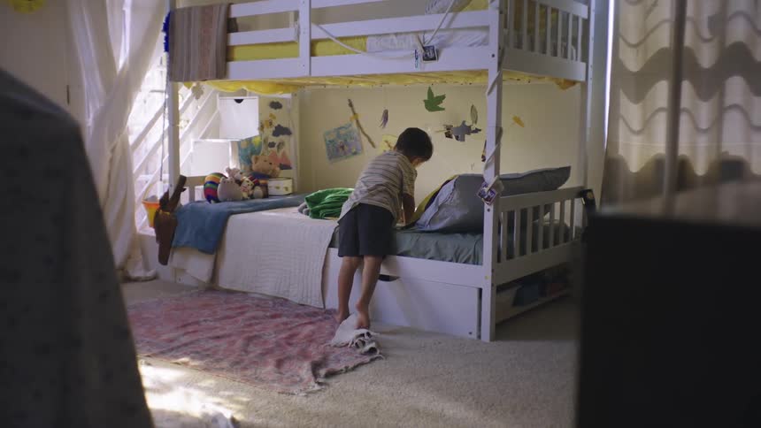 Small child sitting on the bed in his room
