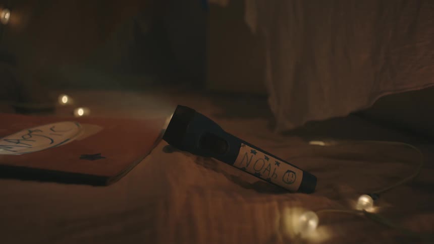 Lit flashlight next to a book with a childs name in a dark room
