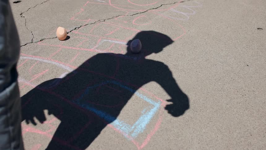 A barefoot boy plays hopscotch outside