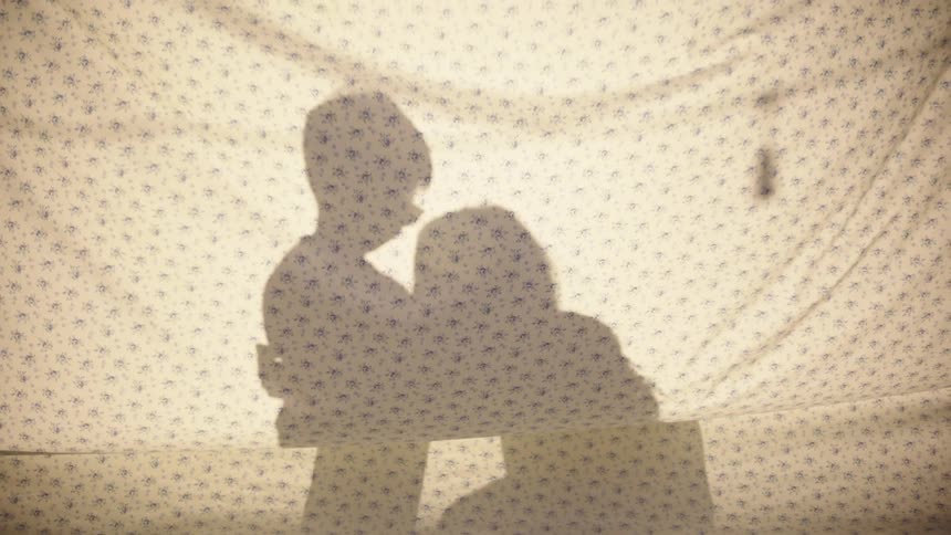 A mother and son embrace outdoors behind a sheet hanging in front of them