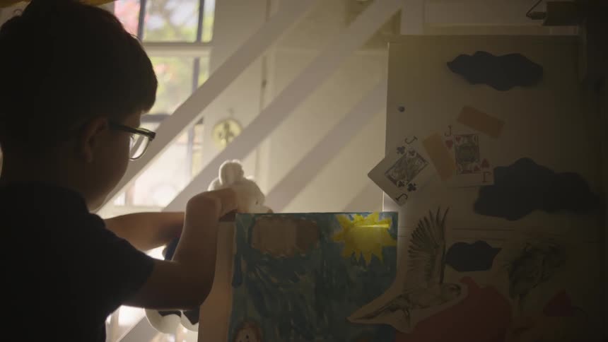 A young boy with glasses plays with a stuffed bear in a bedroom