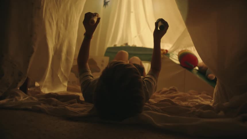 Child lying in a cabin inside the room playing with two flashlights