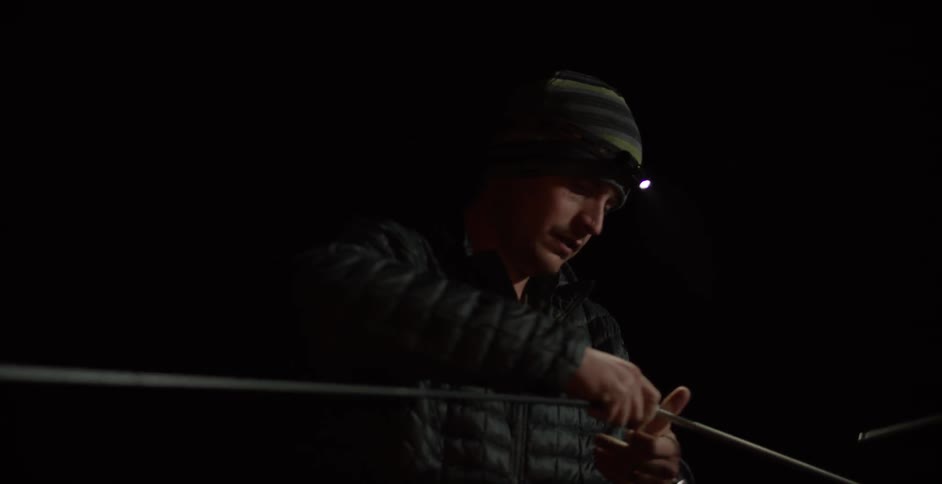 Man using his headlamp to help them see as he ties something together in the dark
