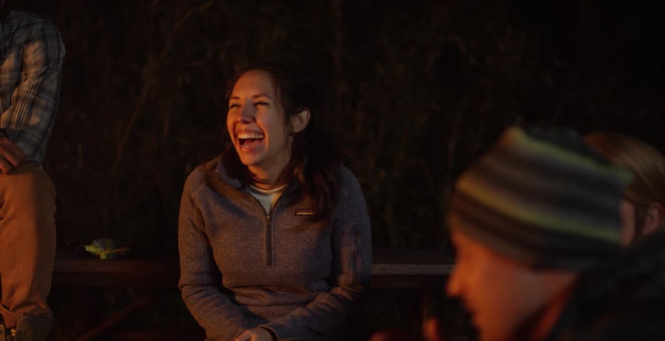 A woman laughs next to a campfire